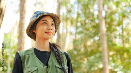 A woman wearing a green vest and hat is looking at the camera. She has long hair. The hat is blue and white