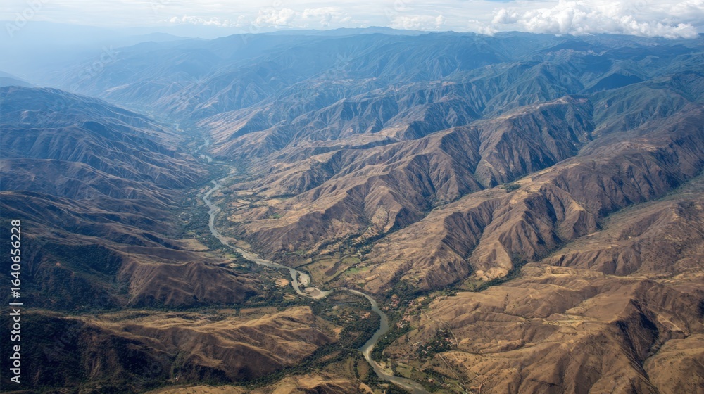 Fototapeta premium Majestic Aerial View of a Winding River Through Mountainous Valley Landscape Under a Hazy Sky