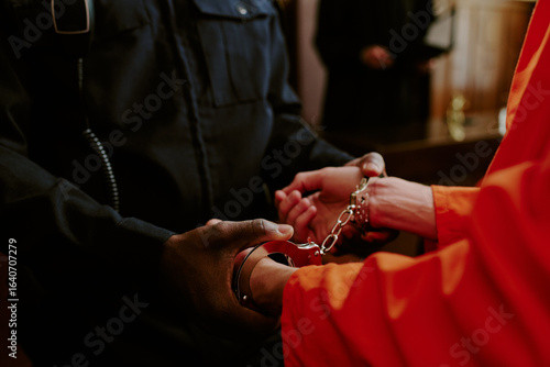 Fotografie Black male police officer handcuffing Caucasian male prisoner in orange jumpsuit