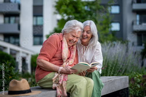 Fotografie Elderly mother sitting on bench with adult daughter, reading book