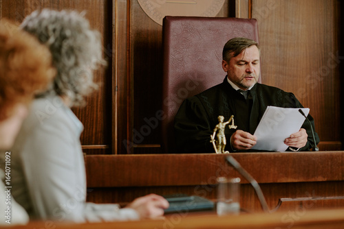 Canvas Print Caucasian middle aged man judge reading legal documents in courtroom while two w