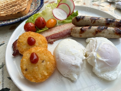 Two poached eggs served with hash brown, pork sausages and bacon