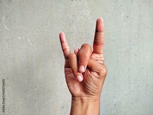 A close-up shot of a hand making the rock on or devil horns  gesture against a neutral gray background.