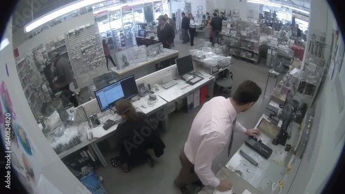 Retail clerk caught with inside-out dress shirt, glancing up at a stationary overhead fisheye surveillance camera