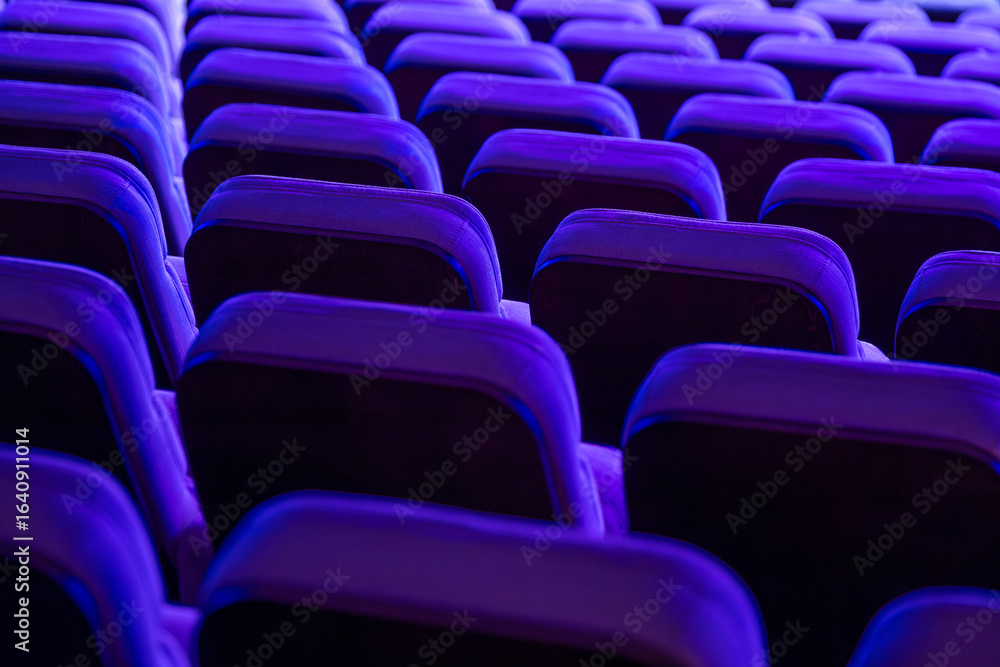Obraz premium Rows of empty theater seats lit by vibrant purple lighting, creating artistic ambiance.