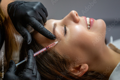 Beautician injects toxin injections in the woman's temple.Woman on cosmetological procedures. Beauty and wellness. Close-up. Plastic surgeon injection filler in temple of woman patien