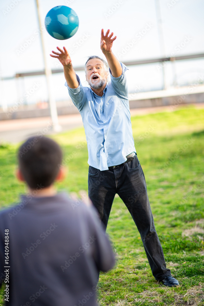 Obraz premium Grandfather enthusiastically throwing ball to grandson during outdoor play