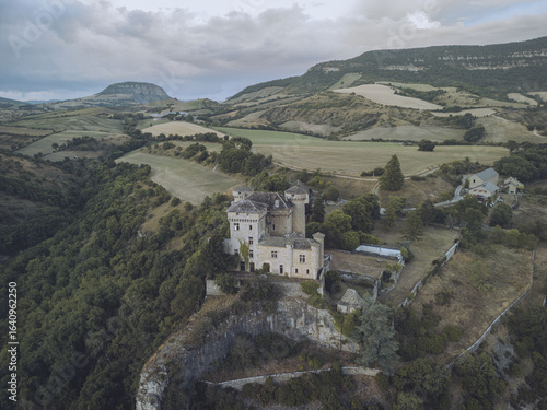 Wallpaper Mural Aerial view of an ancient castle perched on a rugged cliff, overlooking verdant fields and distant plateaus under a muted sky, Chatea de Cabrieres, Occitanie, France. Torontodigital.ca
