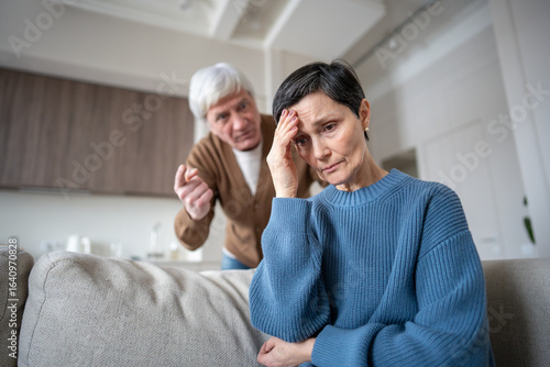 Fotografie Distressed mature wife hiding from yelling husband, enduring aggression from neurotic man in mental instability