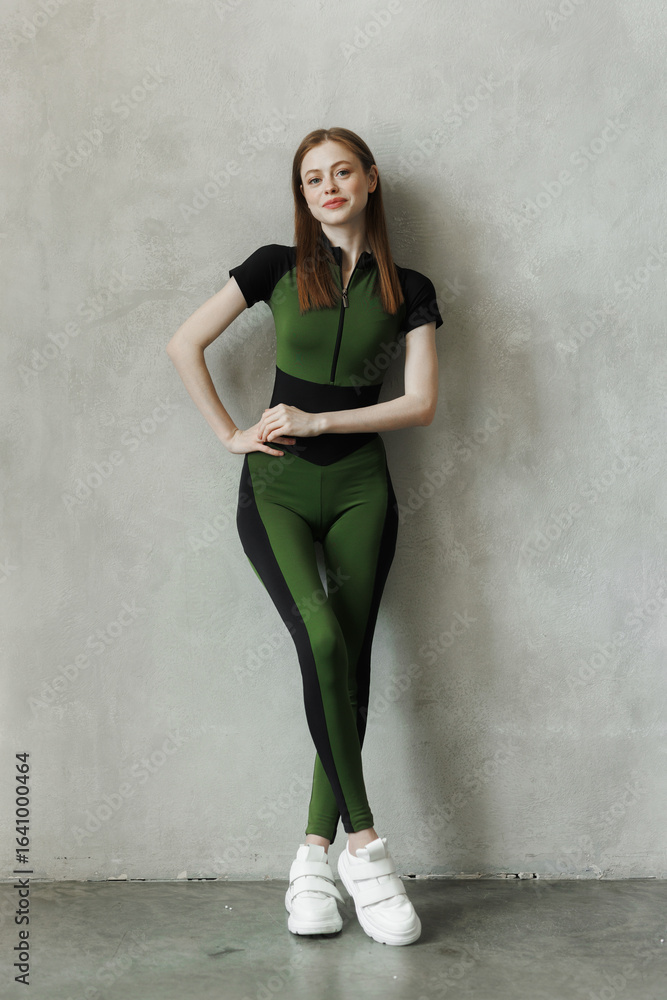 Fototapeta premium young girl in a tracksuit on a wall background. Free space for text. Wide angle vertical wallpaper or web banner.