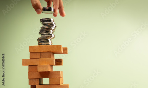 Hand stacks coins atop unstable Jenga tower, symbolizing high risk investments and volatile economic conditions