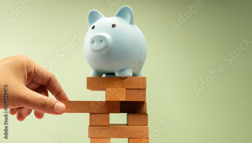 Fotografie piggy bank sits on unstable Jenga tower as a hand carefully removes a piece