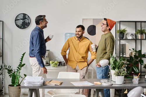 Group of three cheerful South Asian male office workers chatting during coffee break time