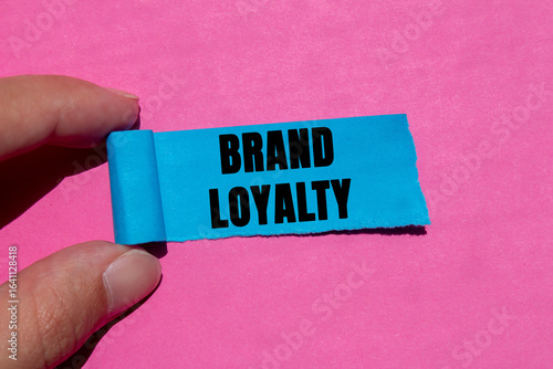 Brand loyalty message written on ripped torn blue paper piece on pink background. Conceptual brand loyalty symbol. Copy space.