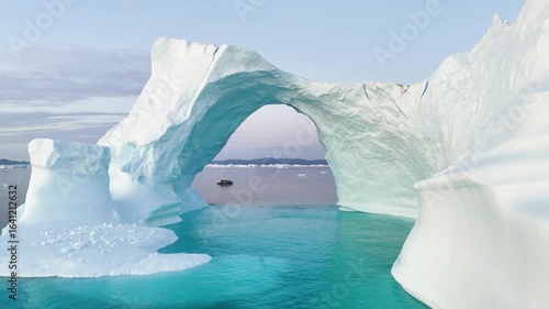 A tall melting iceberg in the Arctic Ocean. A glacier with a huge hole resembling an ice gate. Clear ice floats in turquoise water. Ecology, melting ice, climate change, global warming. Aerial view. 