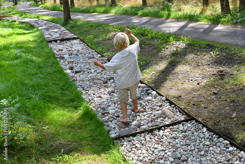 Barefoot boy walking on a sensory trail through a sunny pine forest in summer