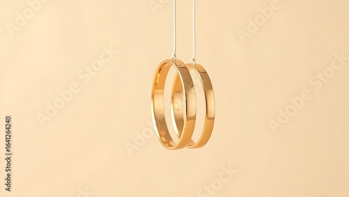 Three golden wedding bands suspended vertically against a soft beige backdrop.