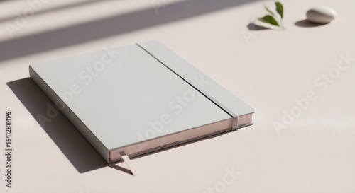 A minimalist light gray notebook with a pink edged paper stack and elastic band sits on a light surface
