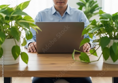 Man working on laptop surrounded by lush green plants in a bright modern office setting