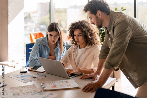 Marketing team analyzing data and collaborating on laptop in office meeting