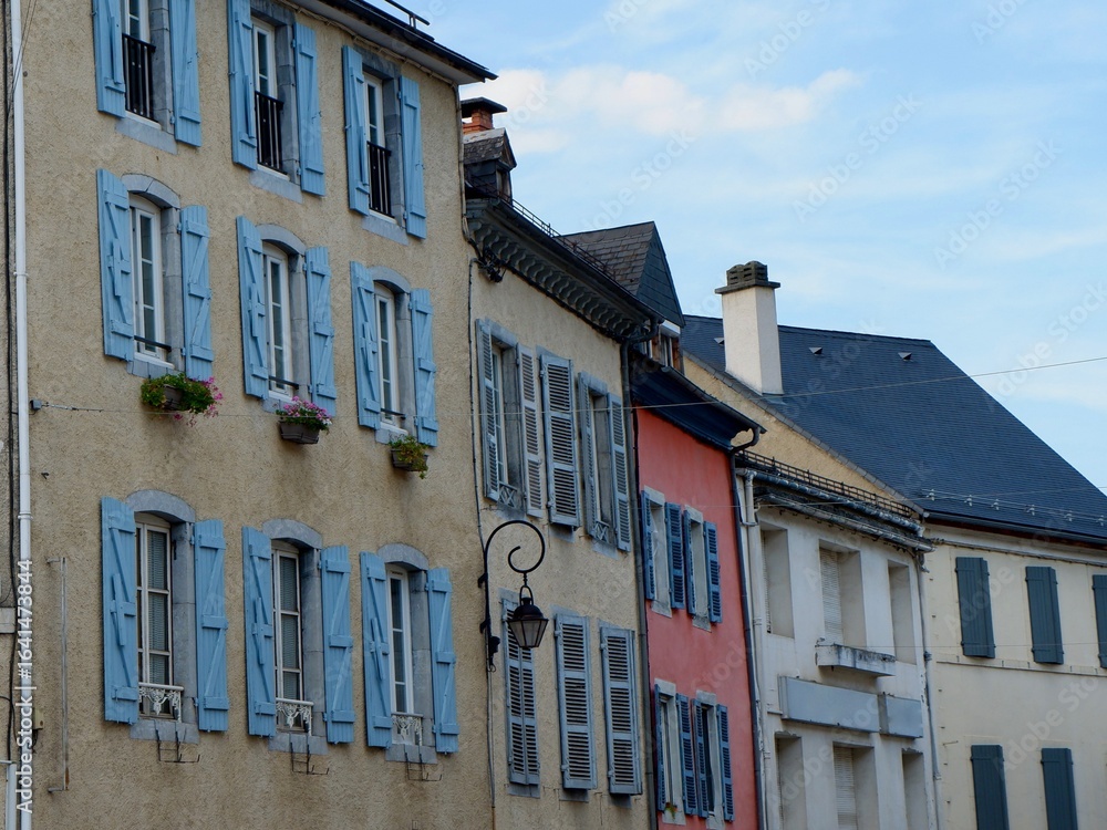 Naklejka premium Quaint buildings featuring blue shutters and colorful facades line the street in a tranquil French town