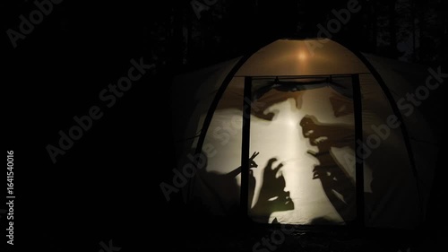 Silhouettes of children create playful shadow puppets inside a glowing tent during nighttime in the forest, capturing a fun and creative moment of outdoor adventure