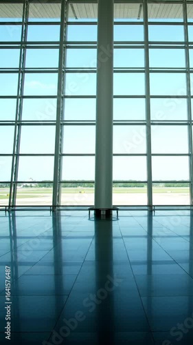 Modern airport terminal waiting area with large glass windows overlooking the runway Empty and spacious hall with reflective floors and a bright sunny day view