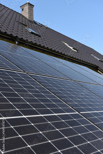 Close-up of photovoltaic panels installed on a house roof, with rural landscape in the background on a sunny summer day