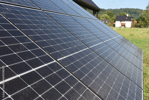 Close-up of photovoltaic panels installed on a house roof, with rural landscape in the background on a sunny summer day