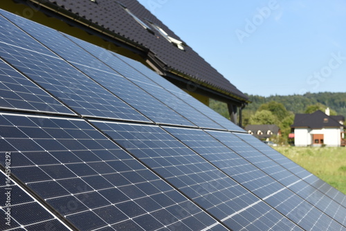 Close-up of photovoltaic panels installed on a house roof, with rural landscape in the background on a sunny summer day