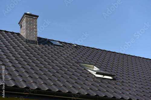 Close-up view of modern tiled roof with chimney and skylights, residential building.