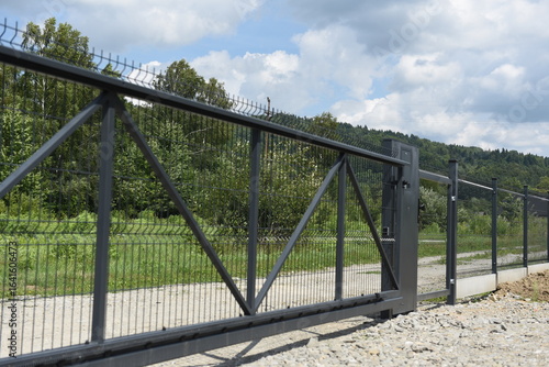 Black sliding gate made of steel with mesh fence along rural road, security concept.