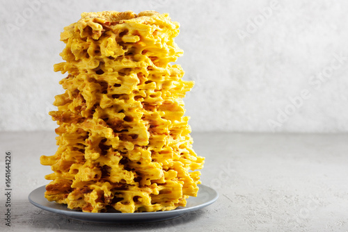 A beautifully baked Sakotis cake stands tall on a gray plate. This traditional Lithuanian tree cake features golden, spiked layers, captured in a minimalist setting with a light gray background