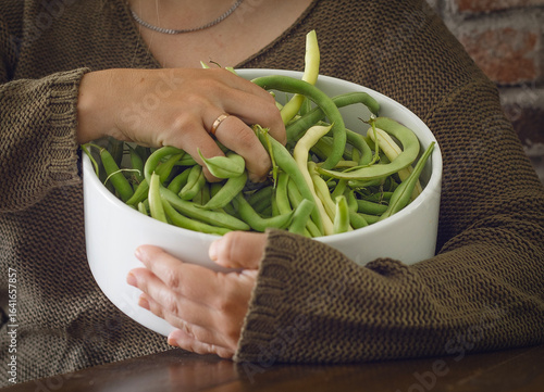 Canvas Print The woman holds a large white bowl filled with fresh green and yellow beans