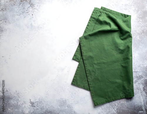 Folded green linen napkin on a mottled gray surface