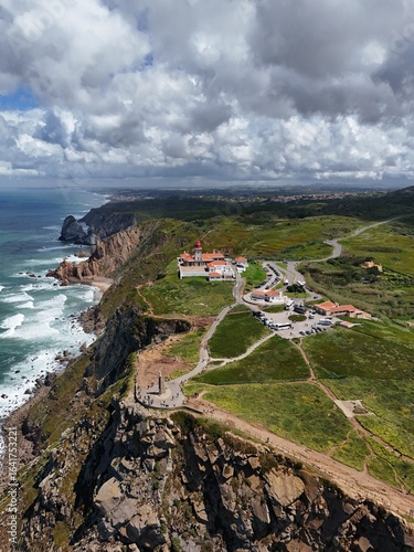 4K Aerial Drone Footage of a Rugged Coastal Landscape Featuring a Lighthouse, Ocean Waves, Cliffs, and Green Hills Captured in Natural Daylight