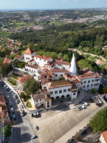 Aerial drone footage showing the historic town of Sintra and the National Palace of Sintra, with red rooftops, green hills, and traditional architecture captured during daylight.