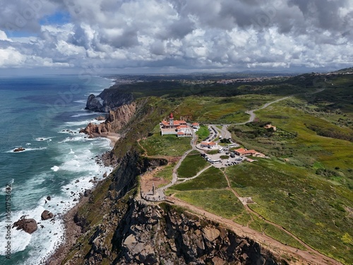 4K Aerial Drone Footage of a Rugged Coastal Landscape Featuring a Lighthouse, Ocean Waves, Cliffs, and Green Hills Captured in Natural Daylight