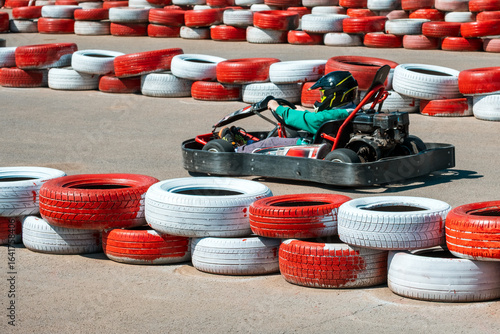 A man is driving a go kart on a track with red and white tires