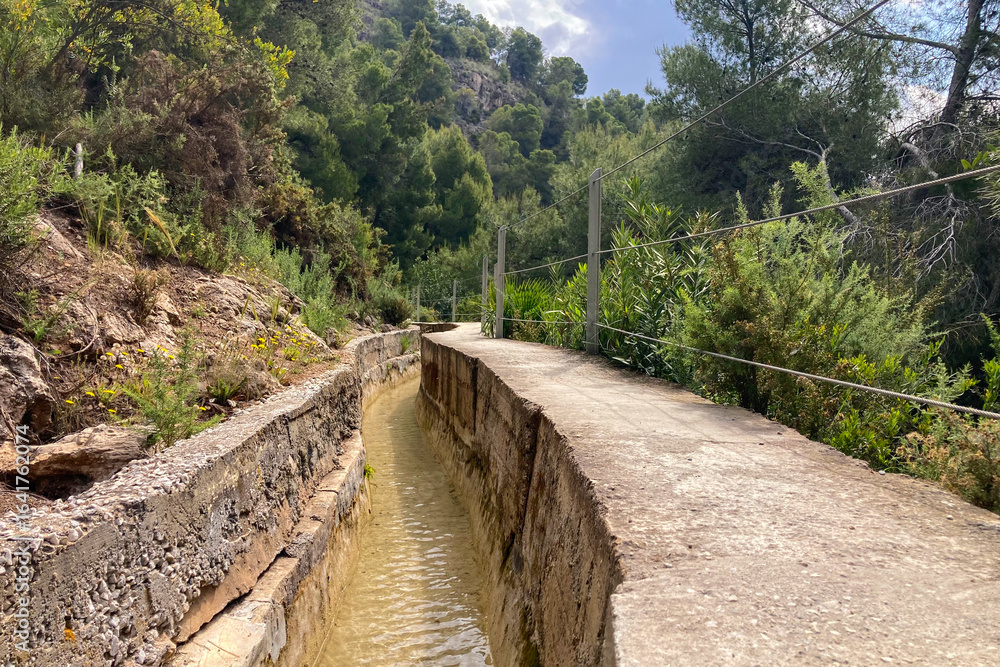 Obraz premium Scenic view of surrounding mountains and picturesque village from a hiking trail along an old irrigation ditch in Frigiliana, Spain.