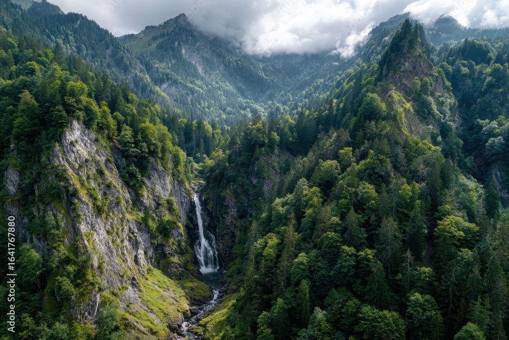Obraz premium Waterfall cascades through lush forested mountains under a cloudy sky in a serene natural landscape