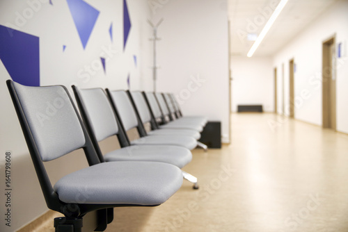 Row of empty gray chairs in bright modern hospital waiting room corridor with clean minimalist interior and doors to doctor offices