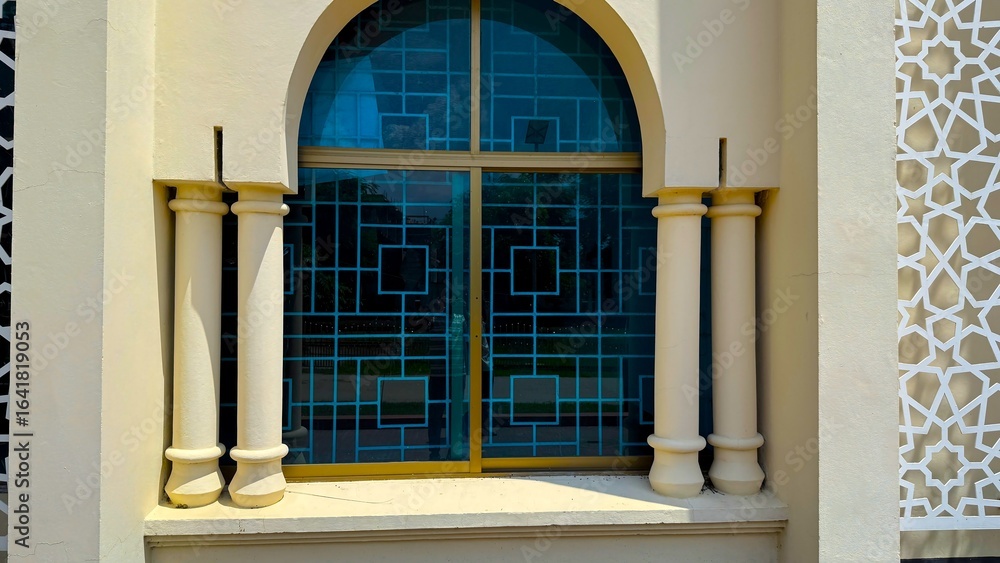 Obraz premium Intricate blue glass window with geometric pattern stands between symmetrical columns outside building