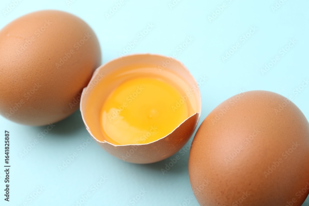 Whole and broken chicken eggs on light blue background, closeup Whole and broken chicken eggs on light blue background, closeup