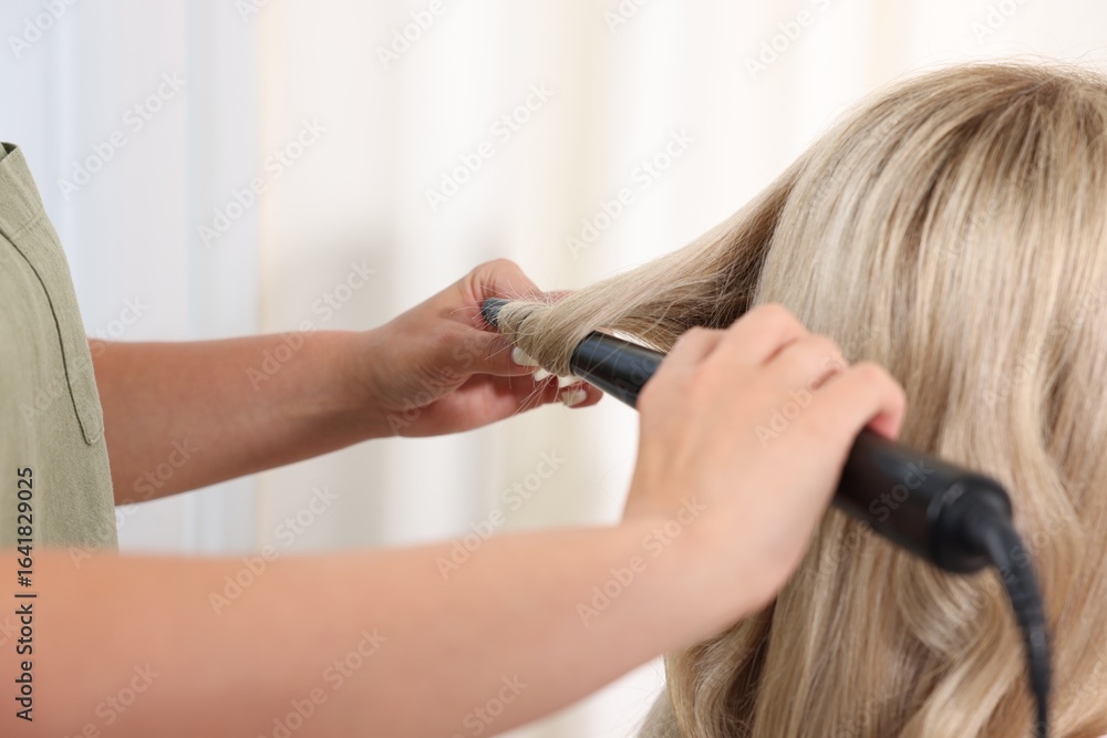 Fototapeta premium Hairdresser curling woman's hair in salon, closeup