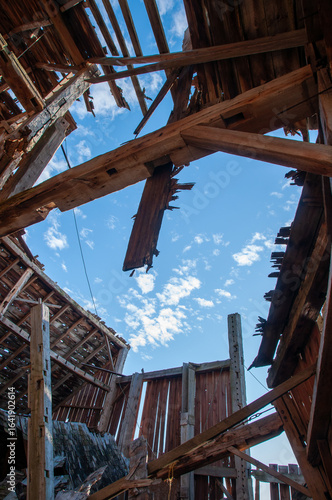 A unique perspective shot from inside a derelict barn, showing the dramatic collapse of the roof with a bright blue sky visible through the gaps.