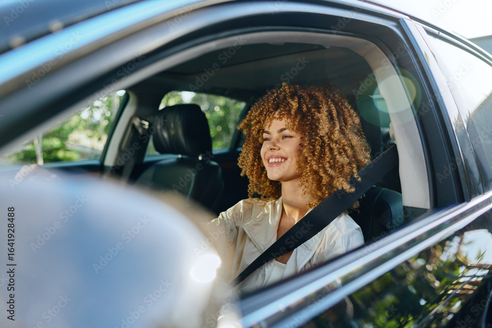 © SHOTPRIME STUDIO - Smiling woman driving car fastened with seatbelt, curly hair, casual clothing, daylight, safe urban travel, joyful expression, natural light. © SHOTPRIME STUDIO - Smiling woman driving car fastened with seatbelt, curly hair, casual clothing, daylight, safe urban travel, joyful expression, natural light.