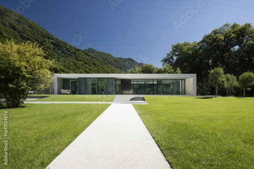Wallpaper Mural A contemporary minimalist home is enveloped by vibrant greenery and majestic mountains, all basking in the warm sunlight of a beautiful day in a stunning landscape Torontodigital.ca
