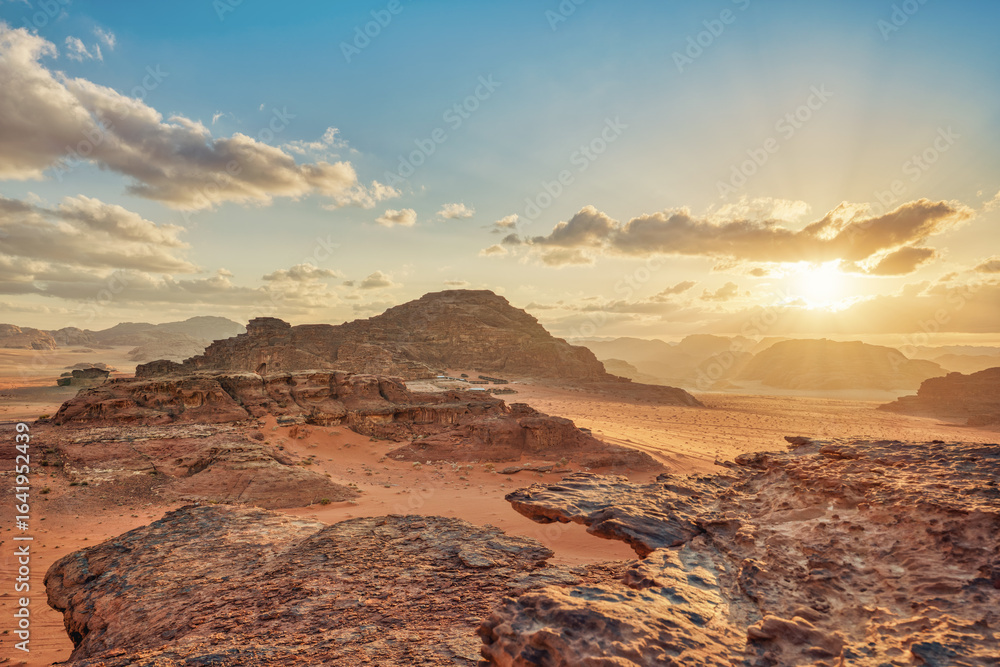 Naklejka premium Morning at Wadi Rum desert, sun rising above rocky mountains terrain in distance, camp tents visible under cliff