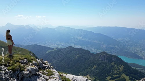 Drone aerial flyby near woman on cliff at La Tournette, Lake Annecy, French Alps, panoramic mountain and lake view, summer travel destination